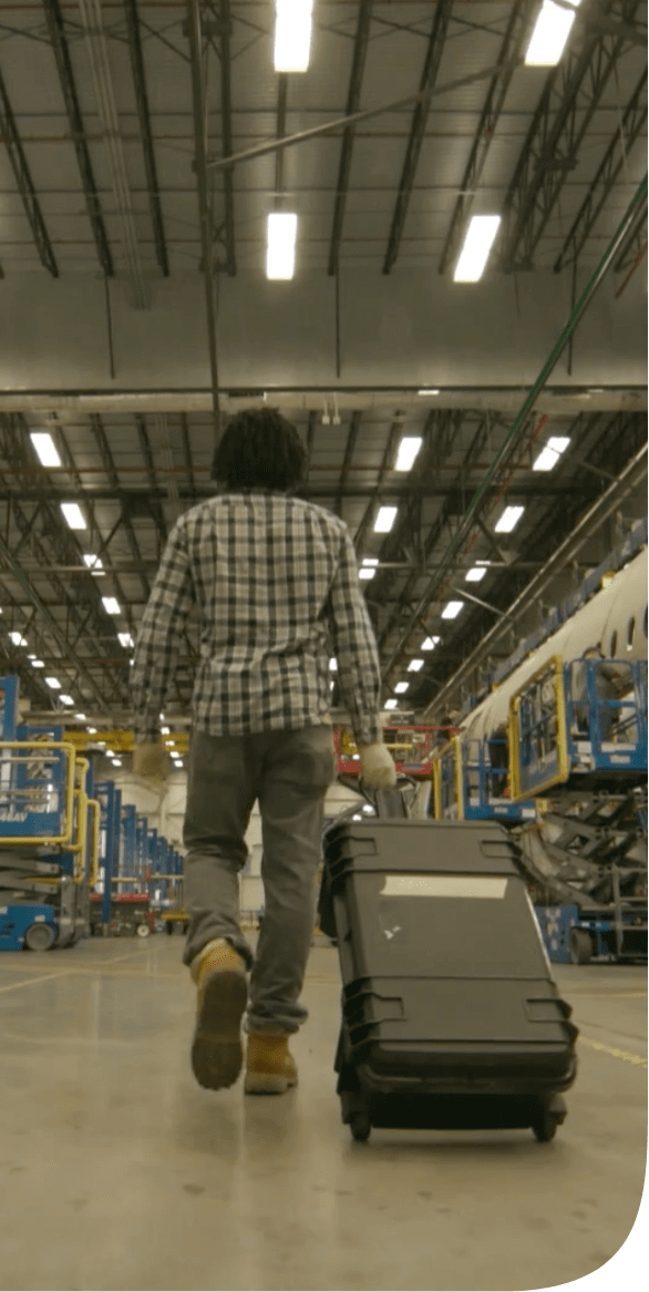 Video still of man walking away with a suitcase in an industrial warehouse.